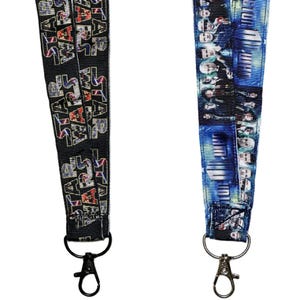 Puede incluir: Dos cordones de tela con cierres de mosquetón de metal. El cordón izquierdo es negro con el texto Star Wars repetido en una fuente multicolor. El cordón derecho presenta un patrón azul y negro con una serie de pequeños retratos.