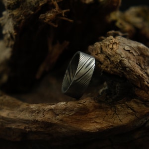 May include: A silver ring with a unique patterned design, resting on a piece of weathered wood.