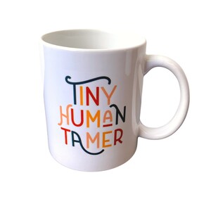 May include: White ceramic mug with the text "Tiny Human Tamer" in colorful lettering. The text is in a playful font with each letter in a different color.