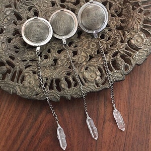 May include: Three silver tea infusers with crystal-shaped handles. The infusers are round with a fine mesh and are hanging from silver chains.