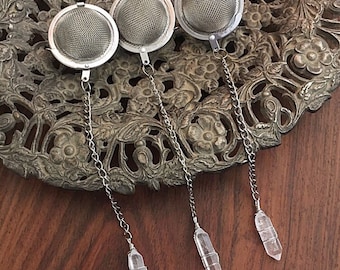 May include: Three silver tea infusers with crystal-shaped handles. The infusers are round with a fine mesh and are hanging from silver chains.
