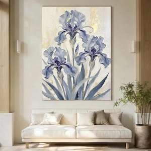 Può includere: Un grande dipinto verticale su tela raffigurante tre fiori di iris blu con petali strutturati e steli verdi. Lo sfondo è di un colore crema neutro con accenti astratti in foglia d'oro applicati in tutta la composizione.