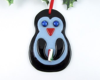 May include: A blue and black glass penguin ornament with red and white candy cane in its beak. The penguin has blue glitter eyes.