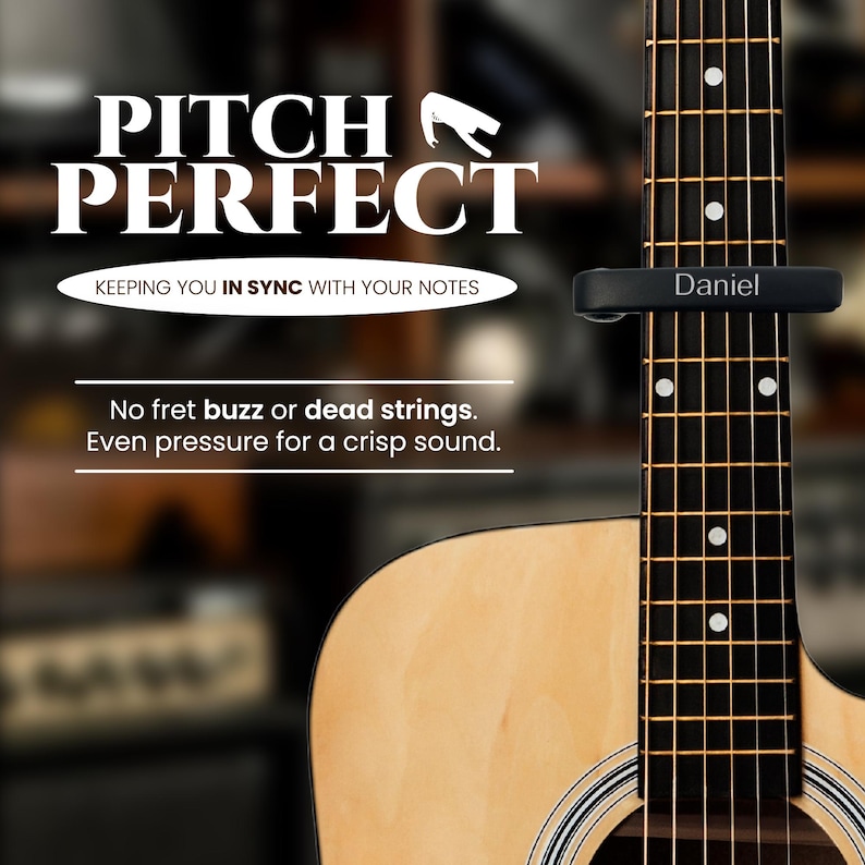 May include: A black guitar capo with the word "Daniel" engraved on it. The capo is attached to the neck of an acoustic guitar. The text "Pitch Perfect" is displayed above the guitar, along with the tagline "Keeping you in sync with your notes".