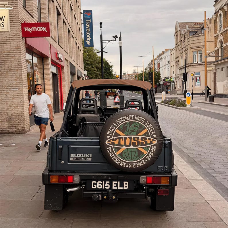 Peut inclure: Un v&eacute;hicule Suzuki gris fonc&eacute; avec une capote marron, dot&eacute; d'une housse de roue de secours avec un graphique de globe et le texte STUSSY, PEACE & PROSPERITY NEGRIL JAMAICA, et STUSSY BEACH BAR N SURF SHACK SINCE 1980. La plaque d'immatriculation est G615 ELB.