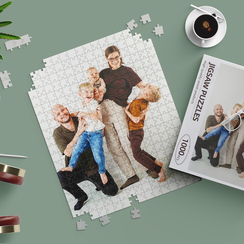 May include: A 1000-piece jigsaw puzzle featuring a family portrait, with the puzzle partially assembled. The box reads "Jigsaw Puzzles" and "High quality wood products". A cup of coffee sits nearby.