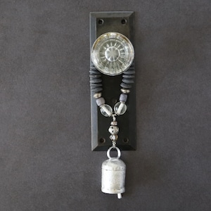 May include: A decorative door knocker with a clear glass knob and a dark metal backplate. A beaded strand with clear and gray beads hangs below, culminating in a silver bell. The design has a rustic, bohemian aesthetic.