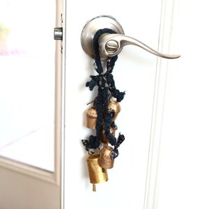 May include: A door handle with a string of gold bells hanging from it. The bells are tied together with a black and white fabric.