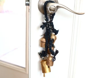 May include: A door handle with a string of gold bells hanging from it. The bells are tied together with a black and white fabric.