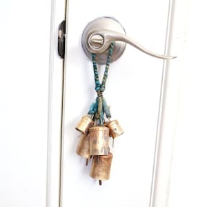 May include: A door handle with a bunch of small gold bells hanging from it. The bells are attached to a blue and green string.