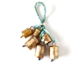 May include: A cluster of small, aged brass bells with a braided loop of blue and green yarn. The bells are attached to the yarn with a thin gold wire. The bells have a rustic, weathered appearance.