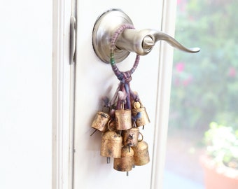 May include: A door handle with a bunch of small gold bells hanging from it. The bells are attached to a colorful string with a knot at the top.