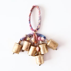 May include: A set of seven small gold bells hanging from a braided cord with colorful yarn tassels.
