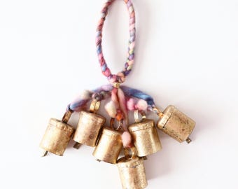 May include: A set of seven small gold bells hanging from a braided cord with colorful yarn tassels.