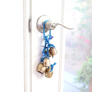 May include: A set of gold-colored bells hanging from a blue rope tied to a silver door handle. The bells are arranged in a cluster and are a popular decorative element for homes.