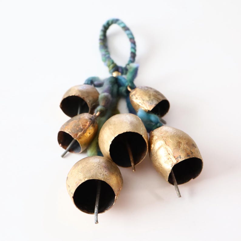 May include: A cluster of gold-colored bells with a blue and green braided cord. The bells are tied together with a blue and green cord and have a small metal loop at the top.