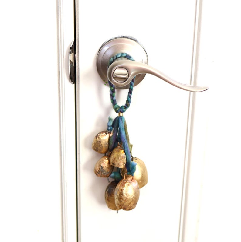 May include: A set of gold bells with a blue and green tassel hanging from a door knob.