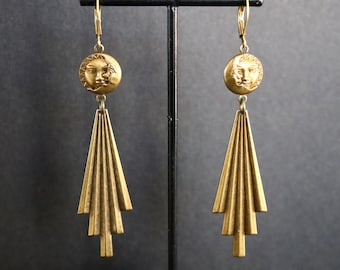 May include: Gold tone earrings with a sun and moon face design and a geometric, fan-shaped dangle.