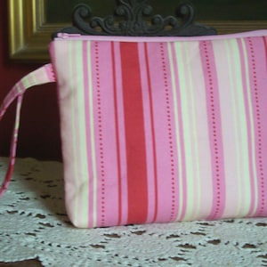 May include: A pink and white striped zippered pouch with a long strap. The pouch is made of fabric and has a dotted pattern.