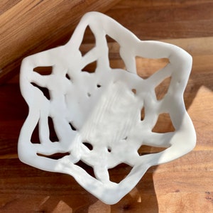 Peut inclure: Bol en céramique blanche avec un design en forme d'étoile et des découpes complexes. Le bol est fait d'un matériau lisse et brillant.