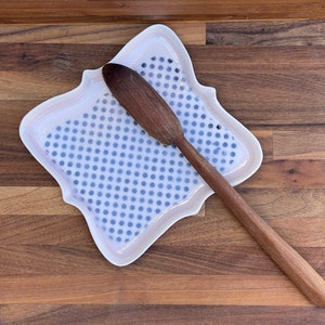Puede incluir: Un plato de cerámica blanco con un patrón de lunares azules y una cuchara de madera descansando encima.