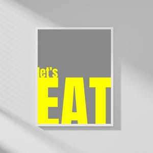 Könnte beinhalten: Ein gerahmter Druck mit den Worten "let's EAT" in leuchtendem Gelb auf grauem Hintergrund. Der Text ist in einer fetten, serifenlosen Schriftart gehalten. Der Rahmen ist weiß, und der Druck wird an einer weißen Wand gezeigt.