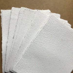 May include: A stack of white handmade paper sheets with a rough, textured surface.