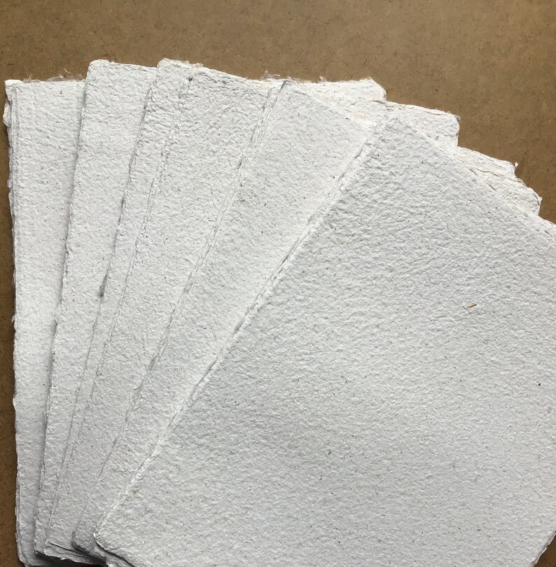 May include: A stack of white handmade paper sheets with a rough, textured surface.