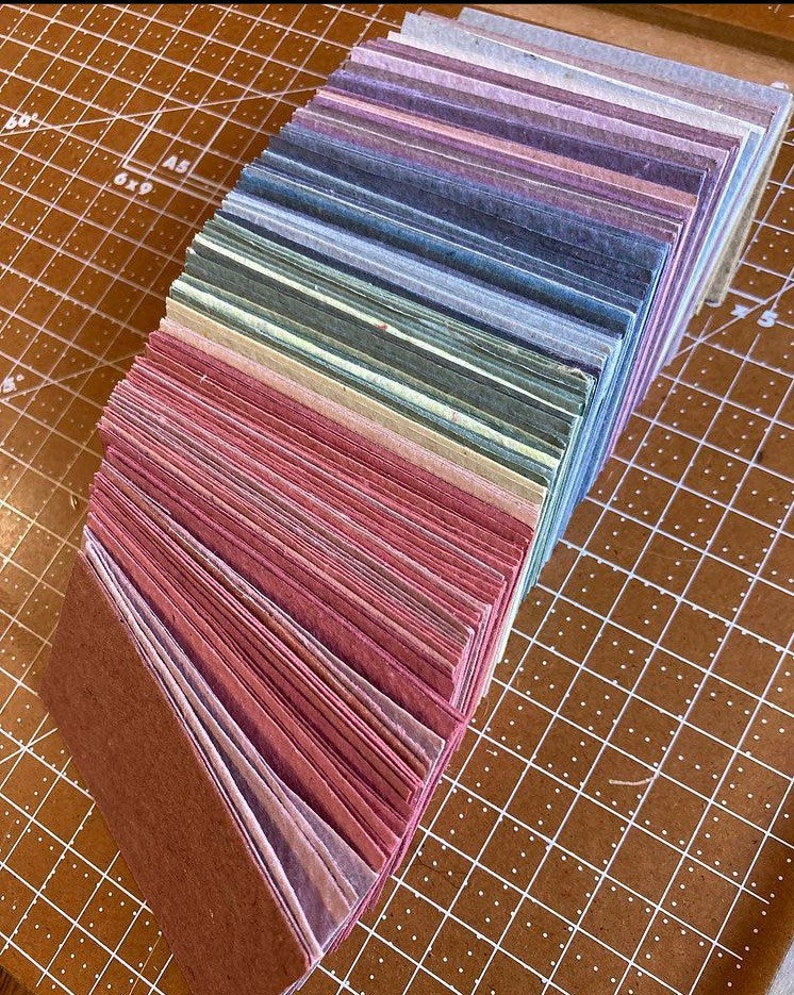 May include: A stack of handmade paper in various shades of pink, purple, blue, green, and brown. The paper is arranged in a rainbow pattern.