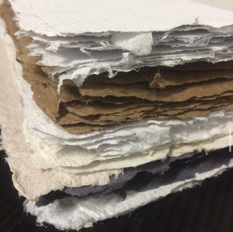 May include: A stack of handmade paper sheets in various shades of white, brown, and grey. The paper has a rough, textured surface and is layered in a staggered pattern.