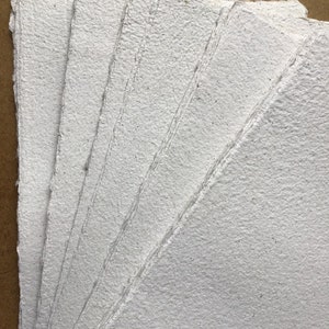 May include: A stack of white handmade paper sheets with a rough, textured surface.