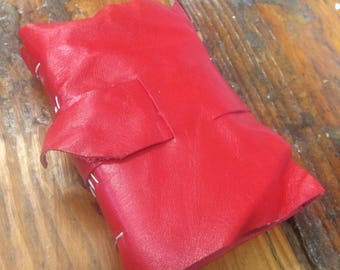 May include: A red leather-bound journal with white stitching. The journal is closed and lying on a wooden surface.