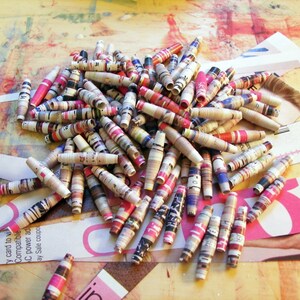 May include: A pile of colorful paper beads made from rolled up magazine pages. The beads are a mix of pink, red, blue, and white.