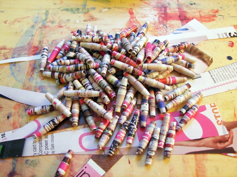 May include: A pile of colorful paper beads made from rolled up magazine pages. The beads are a mix of pink, red, blue, and white.