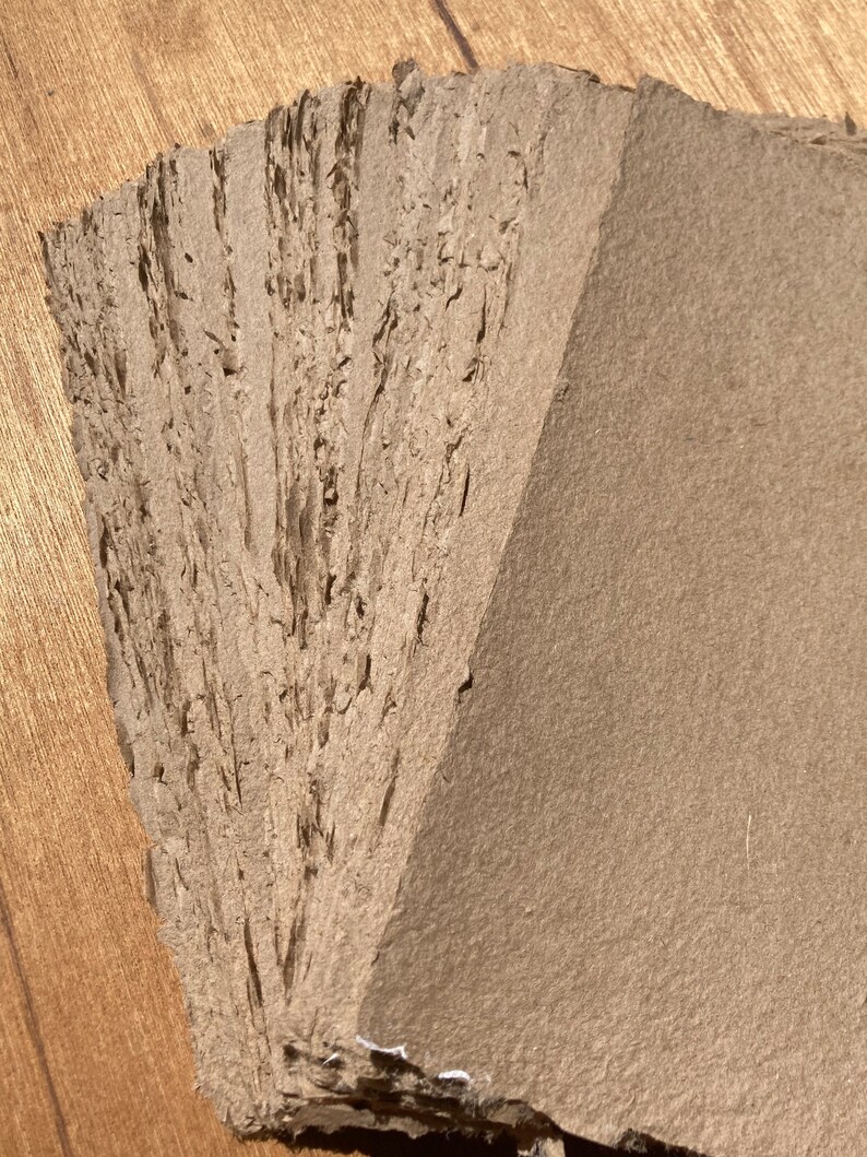 Może przedstawiać: Stos brązowych arkuszy ręcznie robionego papieru o szorstkiej, fakturowanej powierzchni.