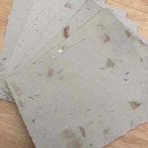 Puede incluir: Una pila de hojas de papel artesanal marr&oacute;n con una textura rugosa y motas de fibras naturales visibles.