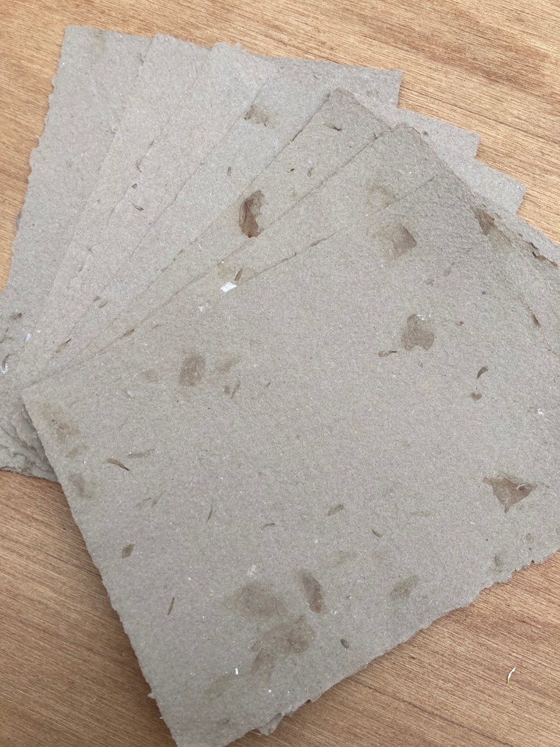 Puede incluir: Una pila de hojas de papel artesanal marr&oacute;n con una textura rugosa y motas de fibras naturales visibles.