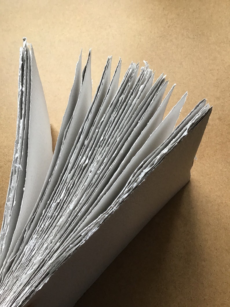 May include: A stack of white paper sheets with rough edges, fanned out in a radial pattern. The paper is slightly textured and appears to be handmade.