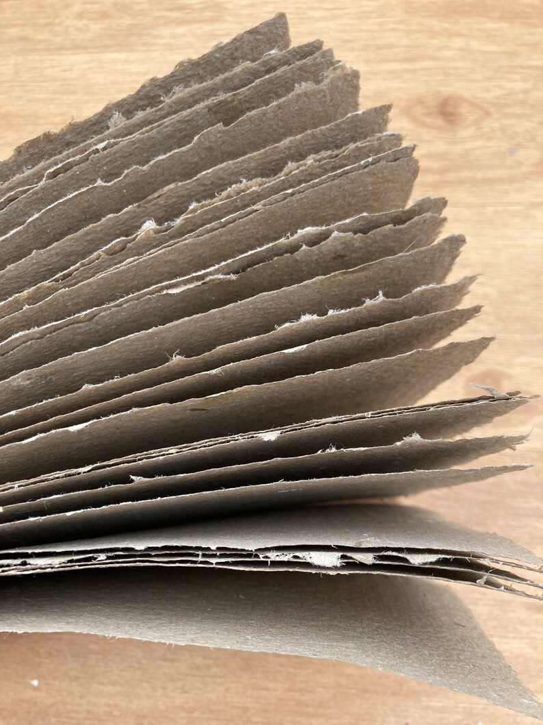 Puede incluir: Una pila de hojas de papel marr&oacute;n con bordes &aacute;speros, que muestran las capas del papel.