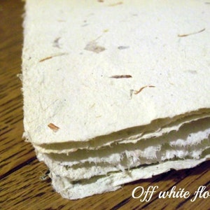 May include: Off-white handmade paper with embedded natural fibers, creating a textured, floral look. The paper is layered, showing the edges of each sheet.