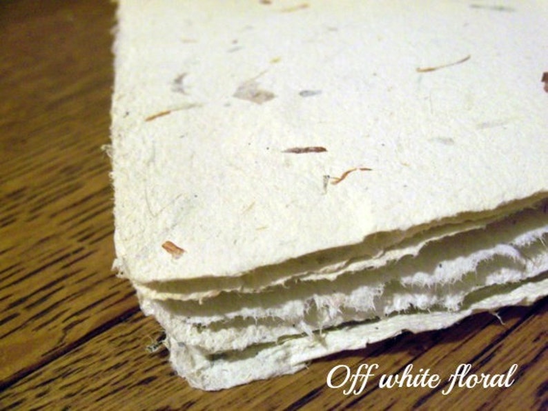 May include: Off-white handmade paper with embedded natural fibers, creating a textured, floral look. The paper is layered, showing the edges of each sheet.