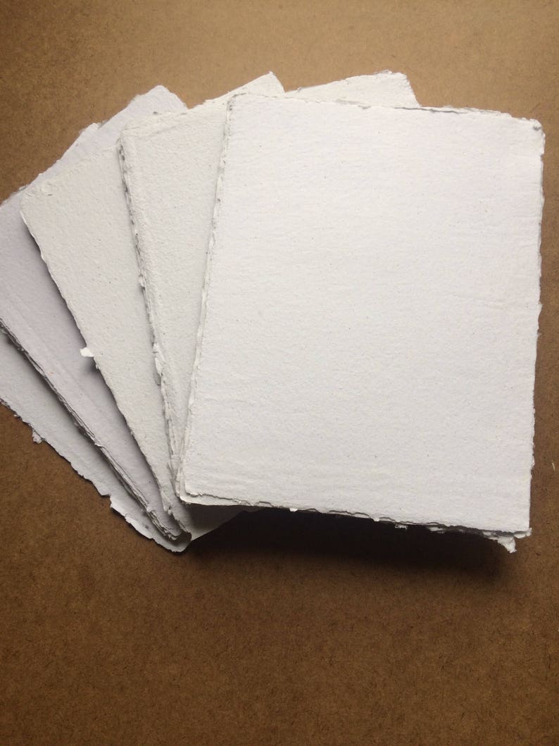 May include: A stack of five white handmade paper sheets with deckled edges. The paper is textured and has a slightly rough surface.