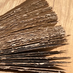 Może przedstawiać: Zbliżenie na stos brązowych arkuszy tektury, pokazujący warstwy i fakturę materiału.