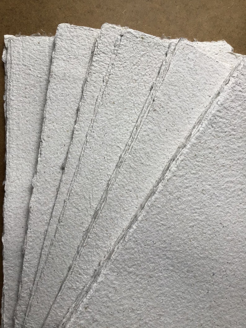 May include: A stack of four white handmade paper sheets with a rough, textured surface.