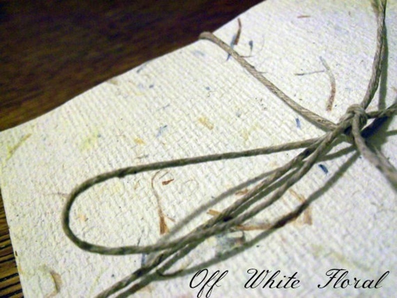 Op de afbeelding: Off-wit papier met een bloemenpatroon en een bruine touw strik.