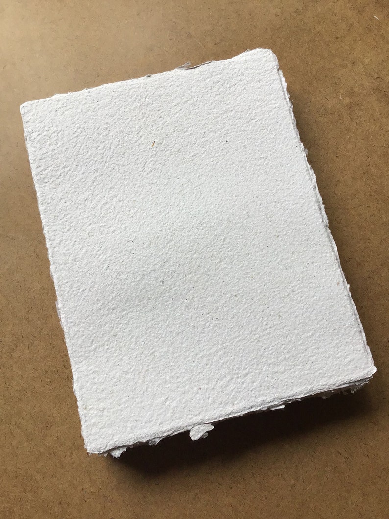 May include: A white handmade paper sheet with a rough, textured surface. The paper has a slightly irregular shape and edges.