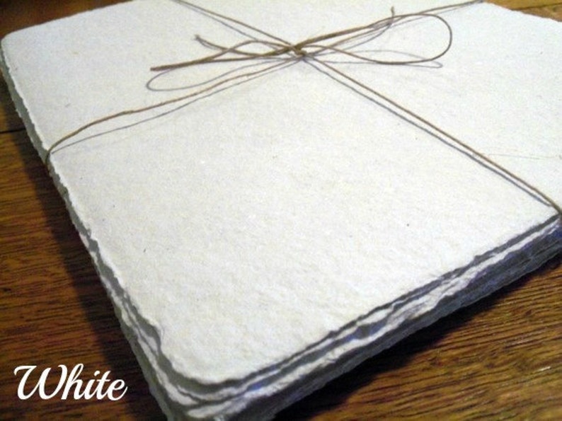 May include: A stack of white handmade paper sheets tied together with twine. The paper has a rough, textured surface.