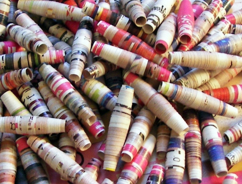 May include: A pile of colorful paper beads made from rolled up magazine pages. The beads are various lengths and have a variety of patterns and colors, including red, blue, green, and yellow.