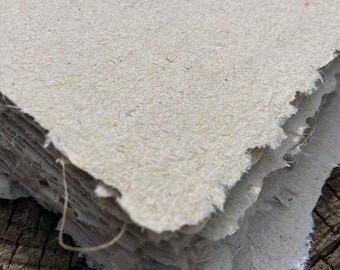 Puede incluir: Una pila de papel hecho a mano con una superficie rugosa y texturizada y bordes deshilachados. El papel es de color beige claro y tiene un aspecto natural y orgánico.