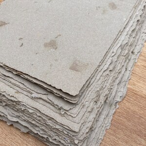 Puede incluir: Una pila de hojas de papel hechas a mano con una superficie rugosa y texturizada de color marr&oacute;n claro. El papel tiene un borde ligeramente irregular y parece estar hecho de materiales reciclados.